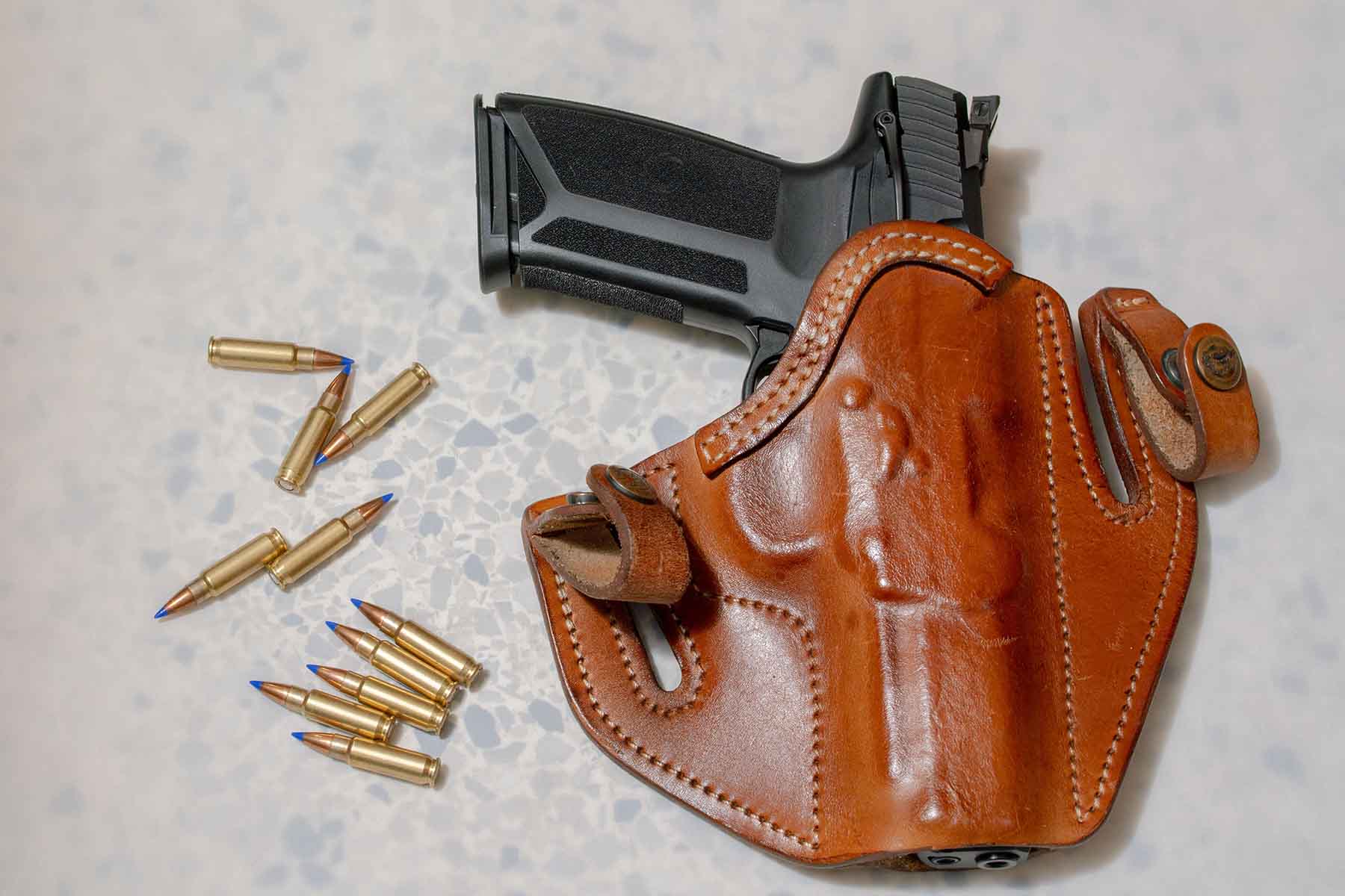 A black handgun inside of a brown leather holster next to several bullets.
