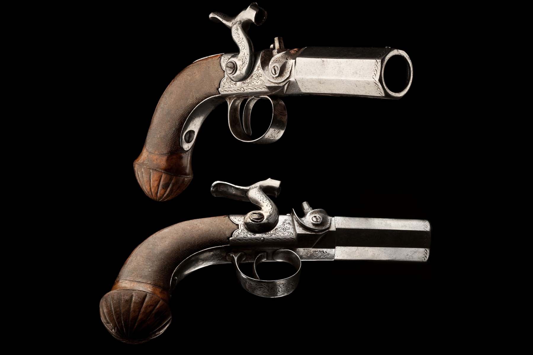 A close-up and artistic shot of two small capsule pistols placed atop each other against a black background.