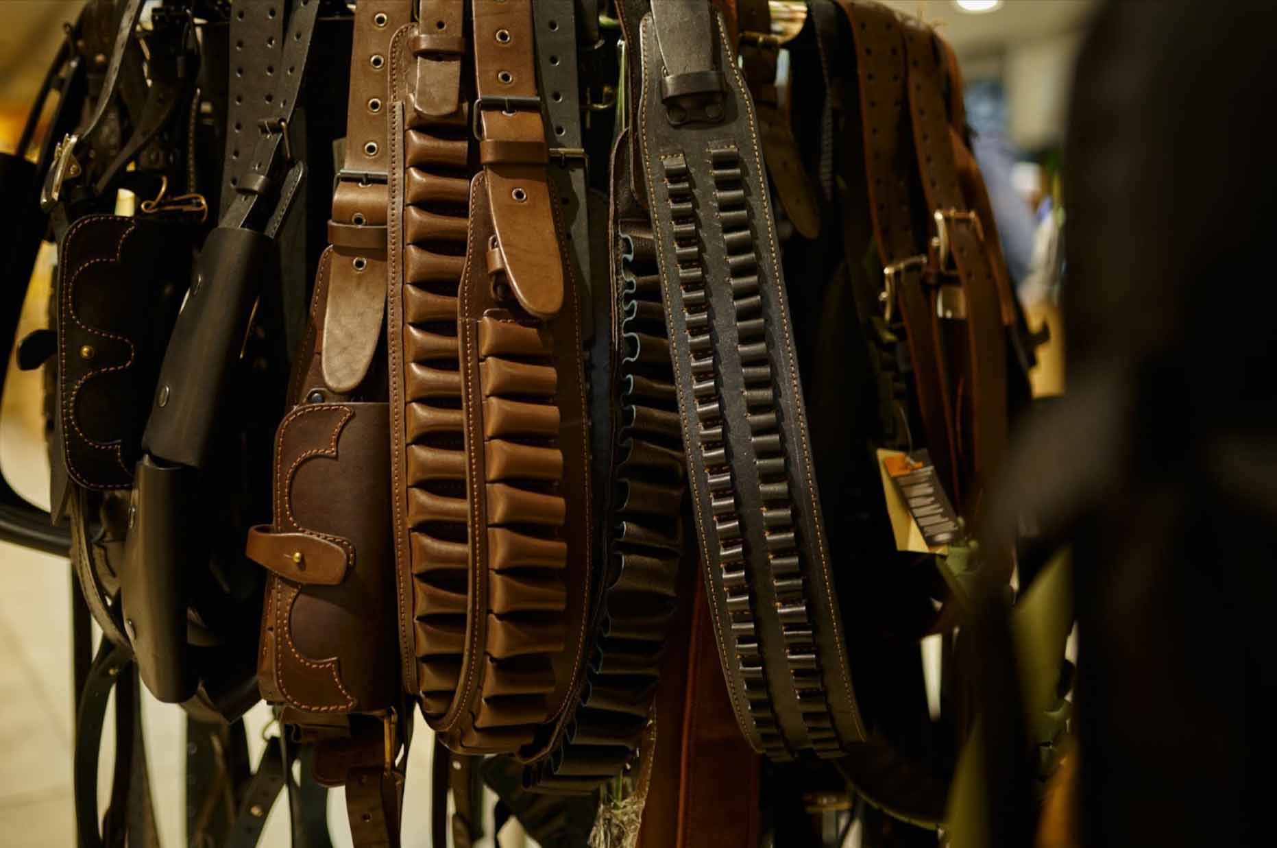 A close-up of various leather bandoliers displayed in a gun store.
