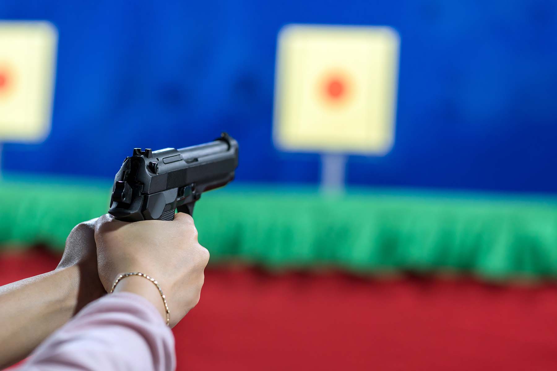 A closeup shot of a woman's arms holding a gun on the shooting range.