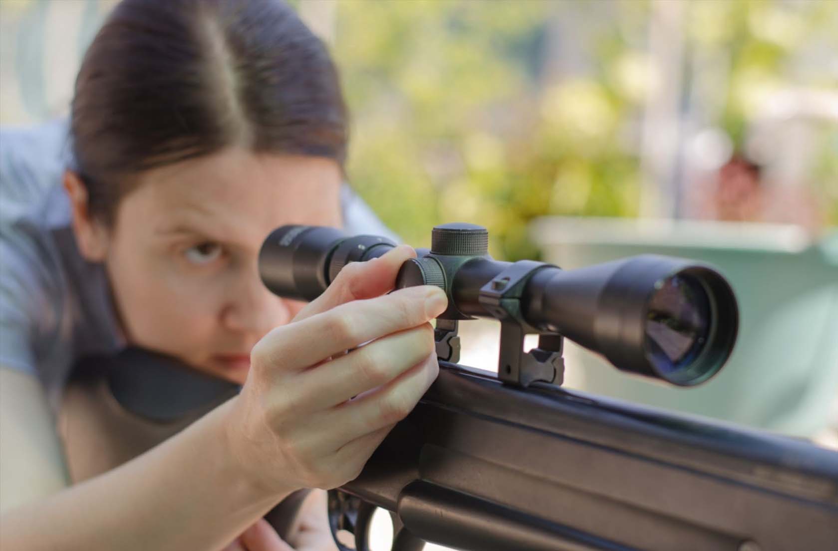 A female sniper carefully calibrates her rifle's scope, peering intently through the optical sight for precision adjustment.
