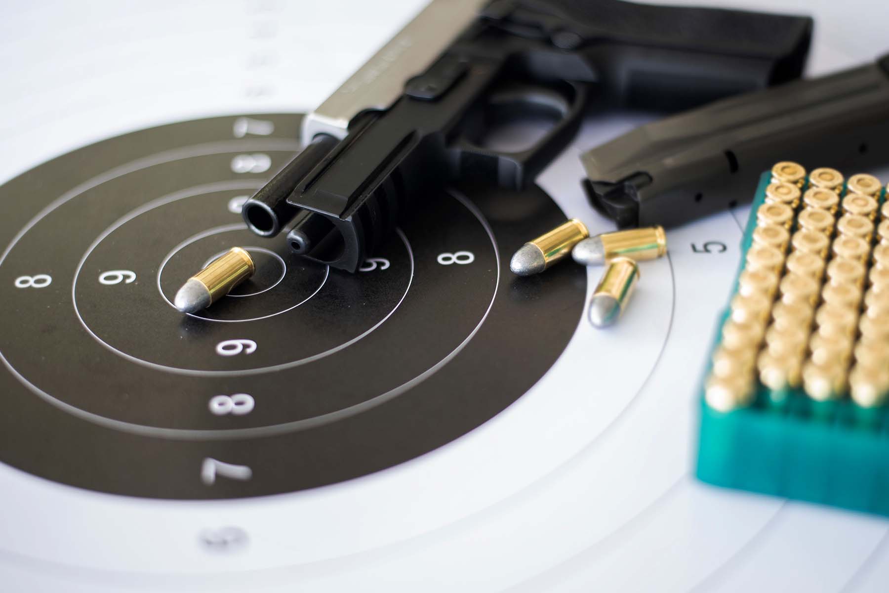 A handgun lying on a target with ammo near it.