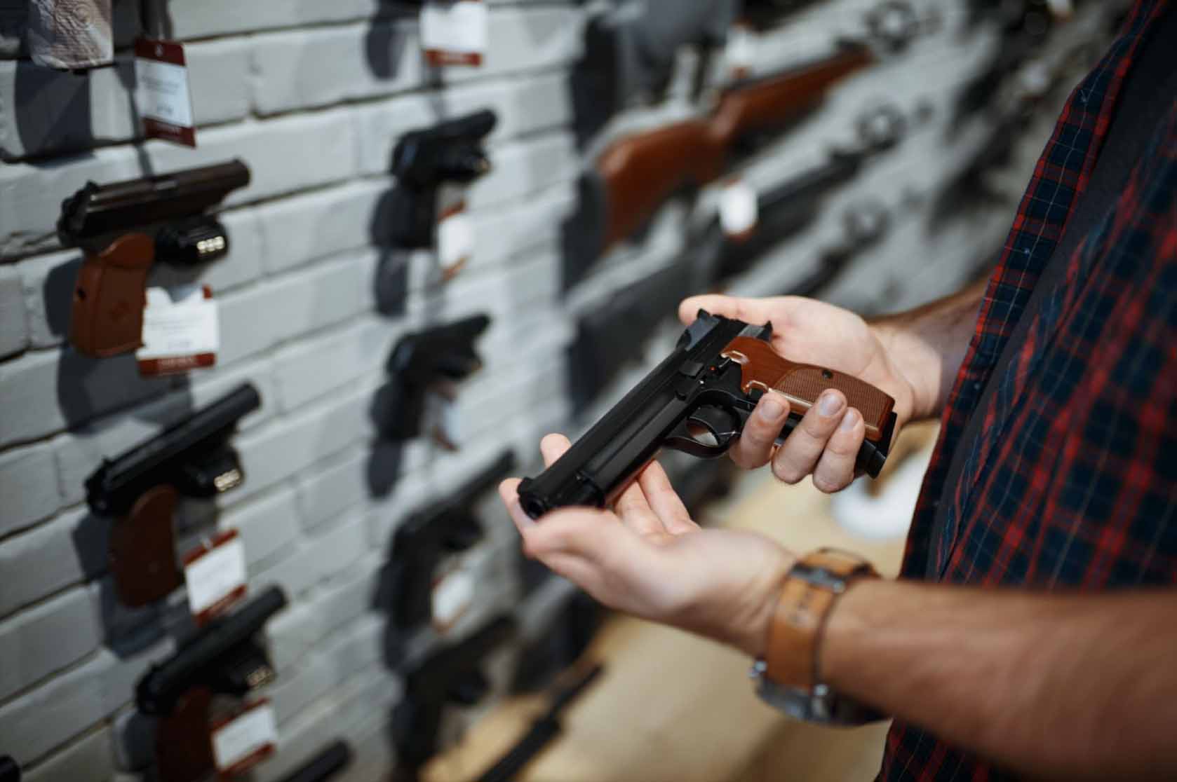 A man evaluating a handgun in front of a gun shop's firearms display.