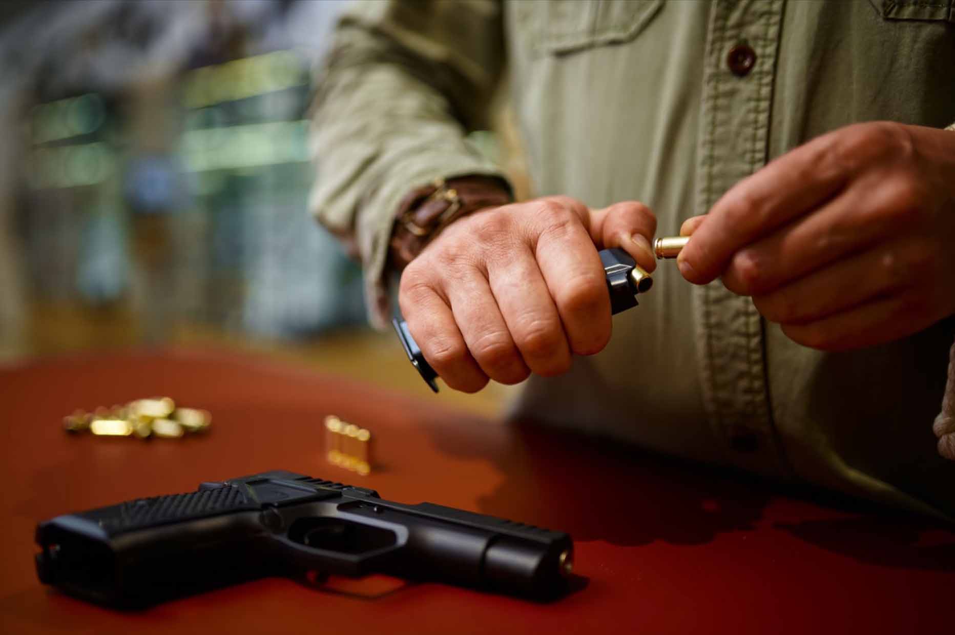 A man loading a magazine with bullets with his gun lying on the table.
