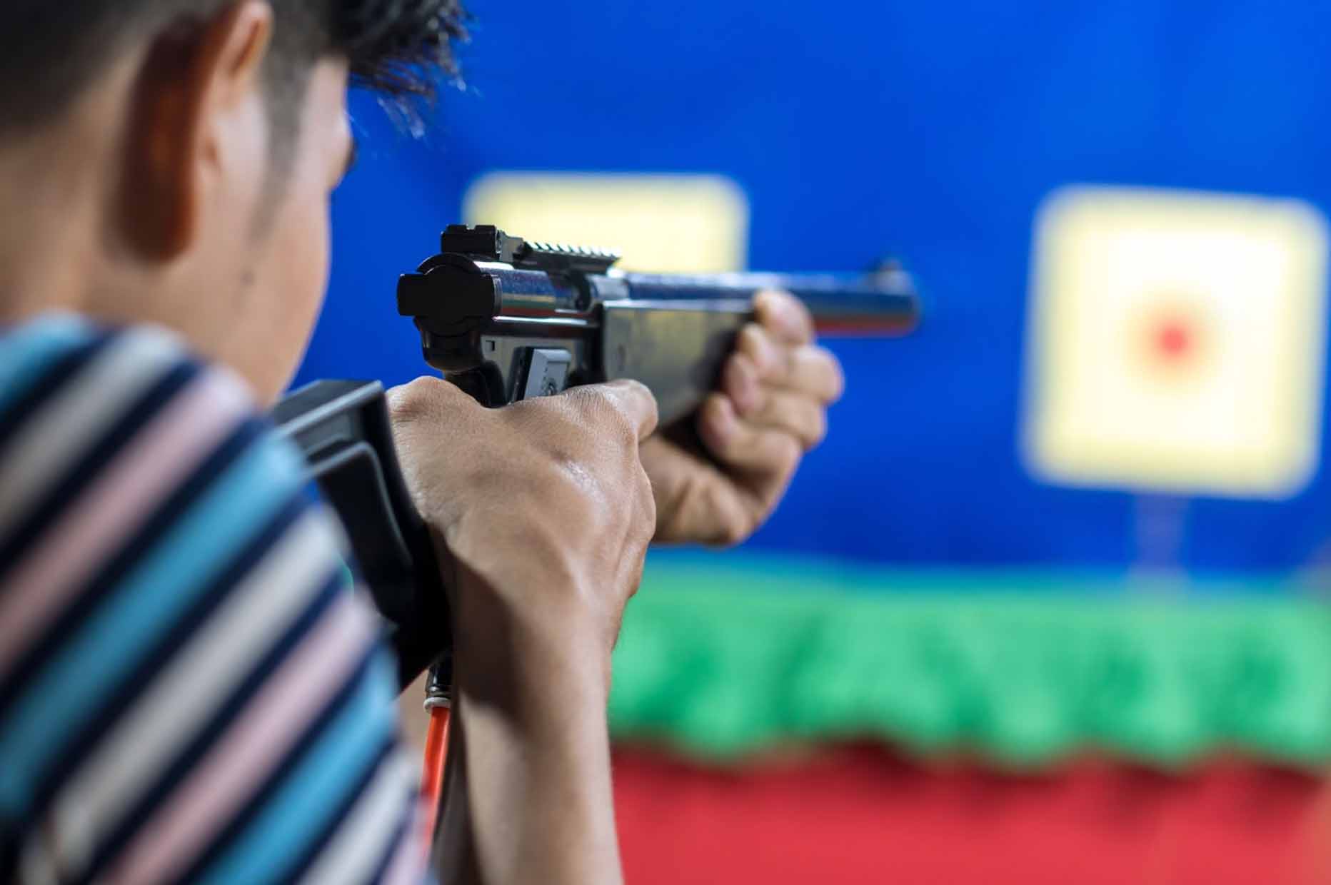 A rear view of a man in a striped shirt aiming his gun at a target in a practice shooting range.