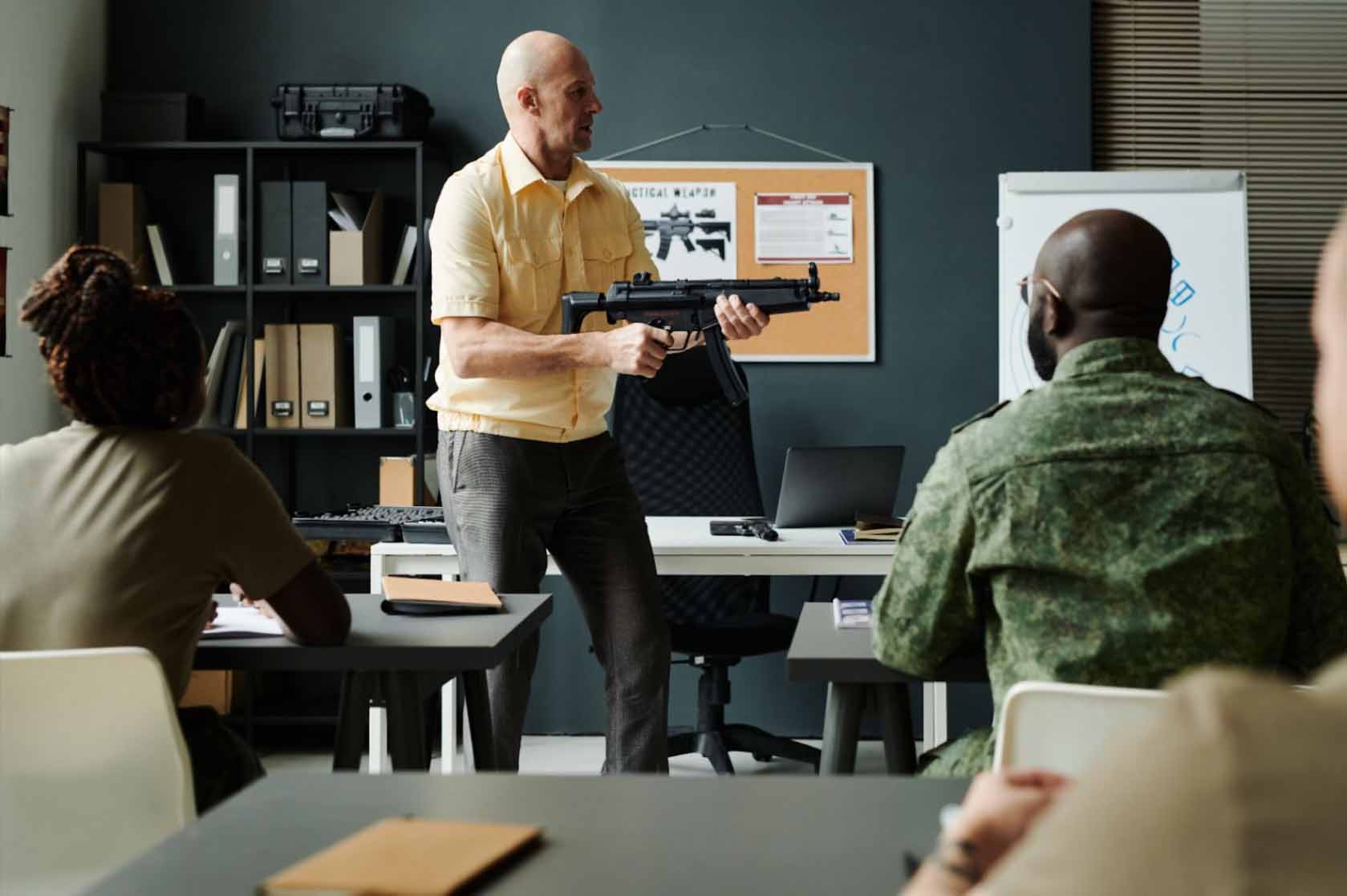 A serious bald instructor teaching the new soldiers proper machine gun shooting techniques.