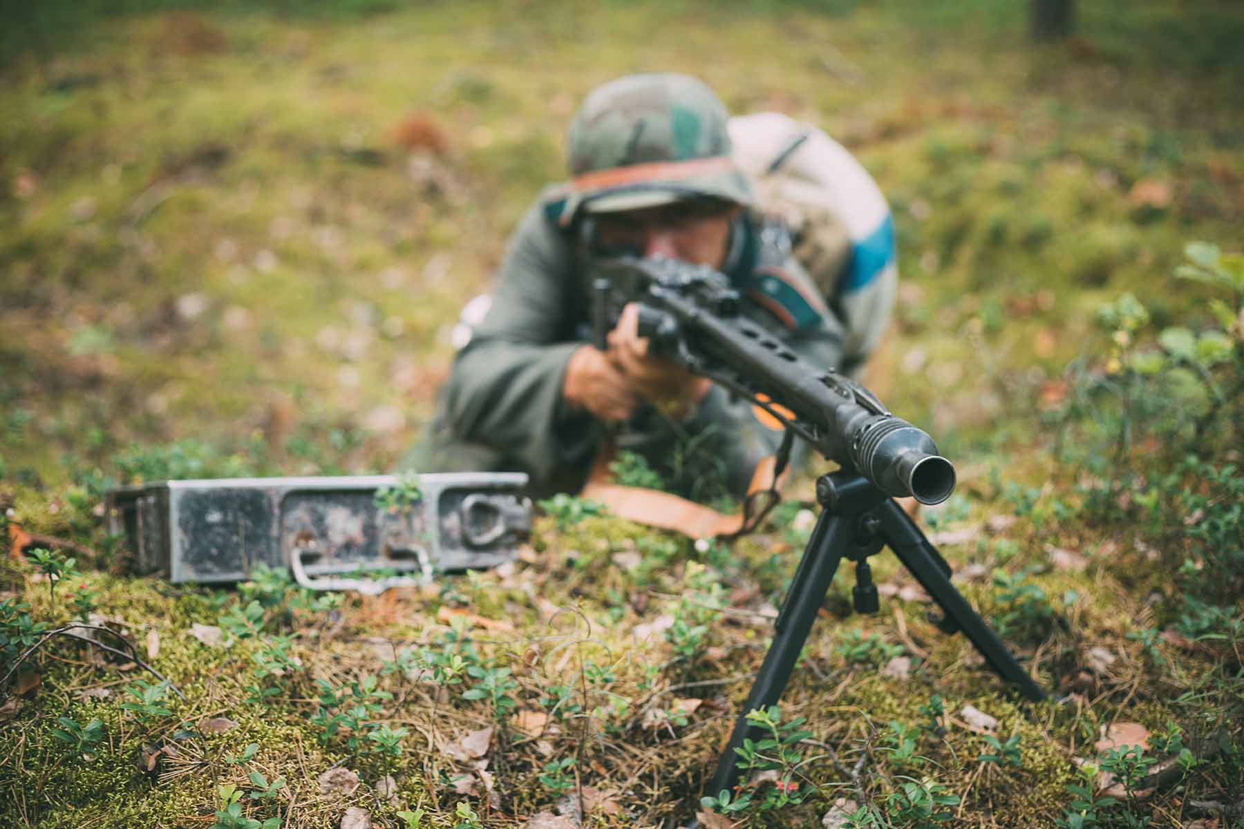 A soldier on the ground aiming a machine gun on top of a gun tripod.