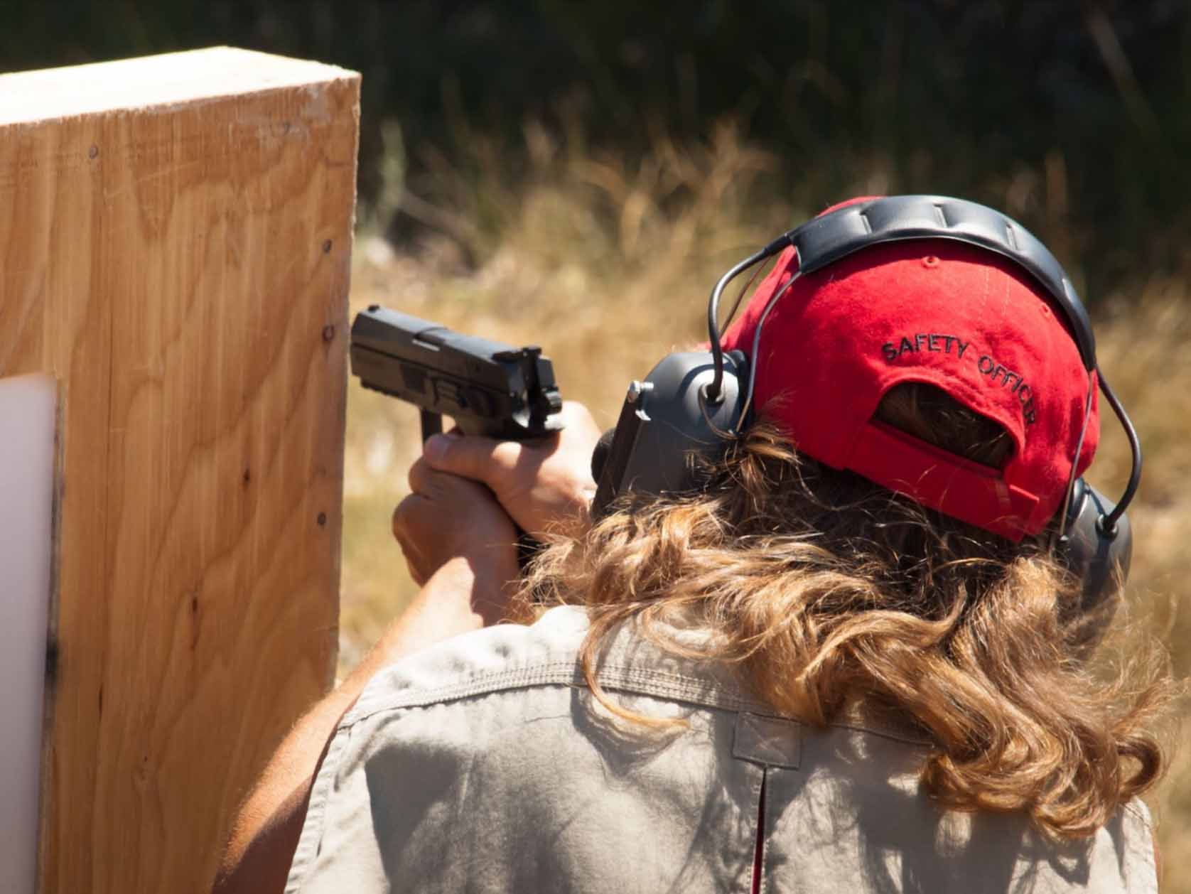 A woman in safety gear aims from behind cover at a shooting competition.