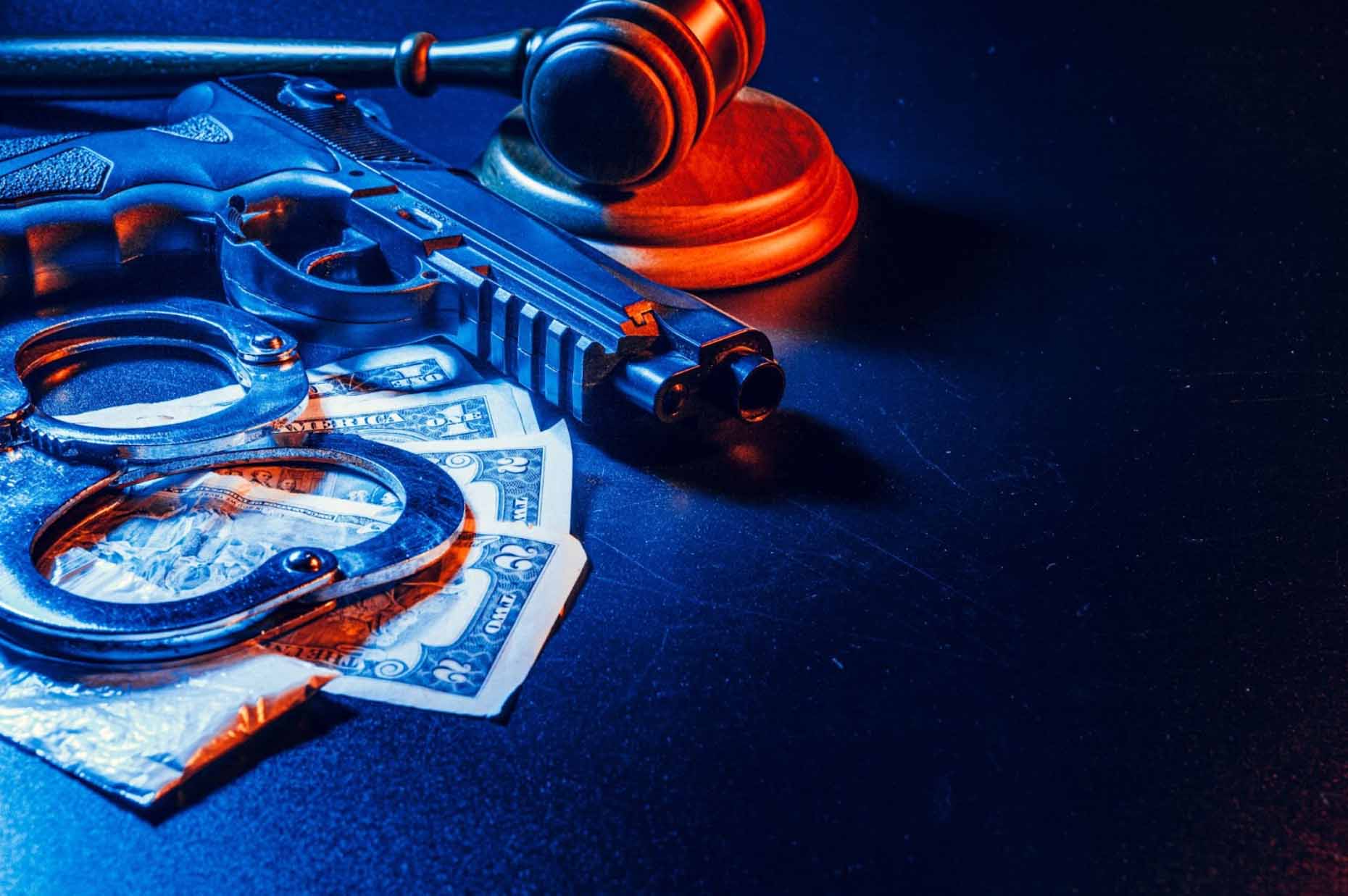A close-up view of a gun, a judge's gavel, handcuffs, and money arranged on a table, symbolizing the intersection of law enforcement and legal judgment.