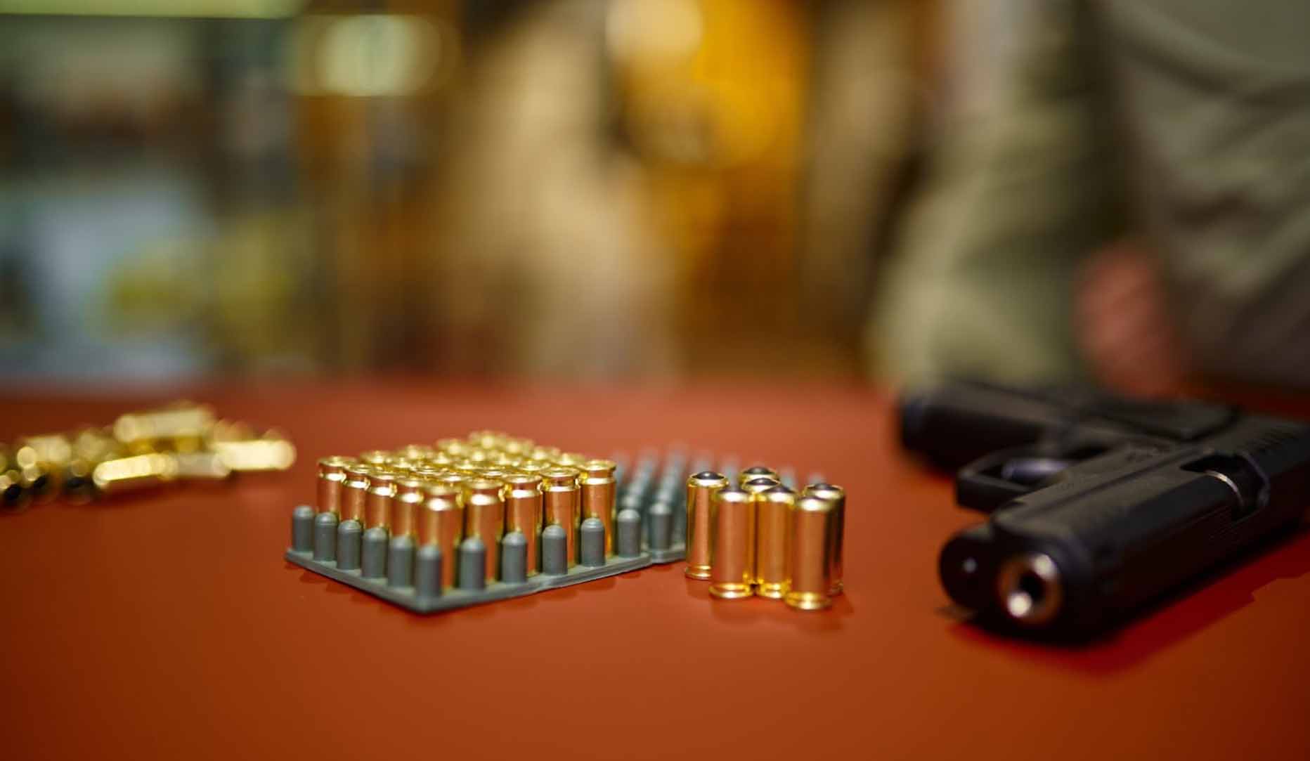 An assortment of bullets lying next to a firearm on a table.