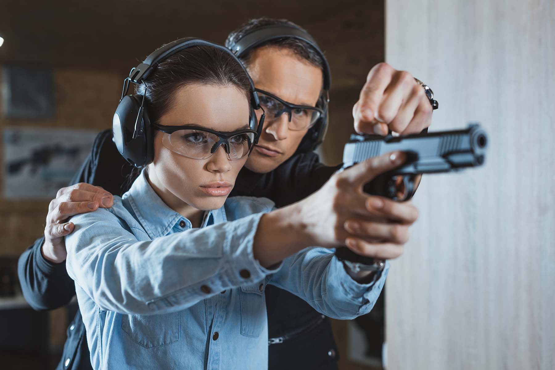 An instructor helping a woman fire her weapon in a shooting range.