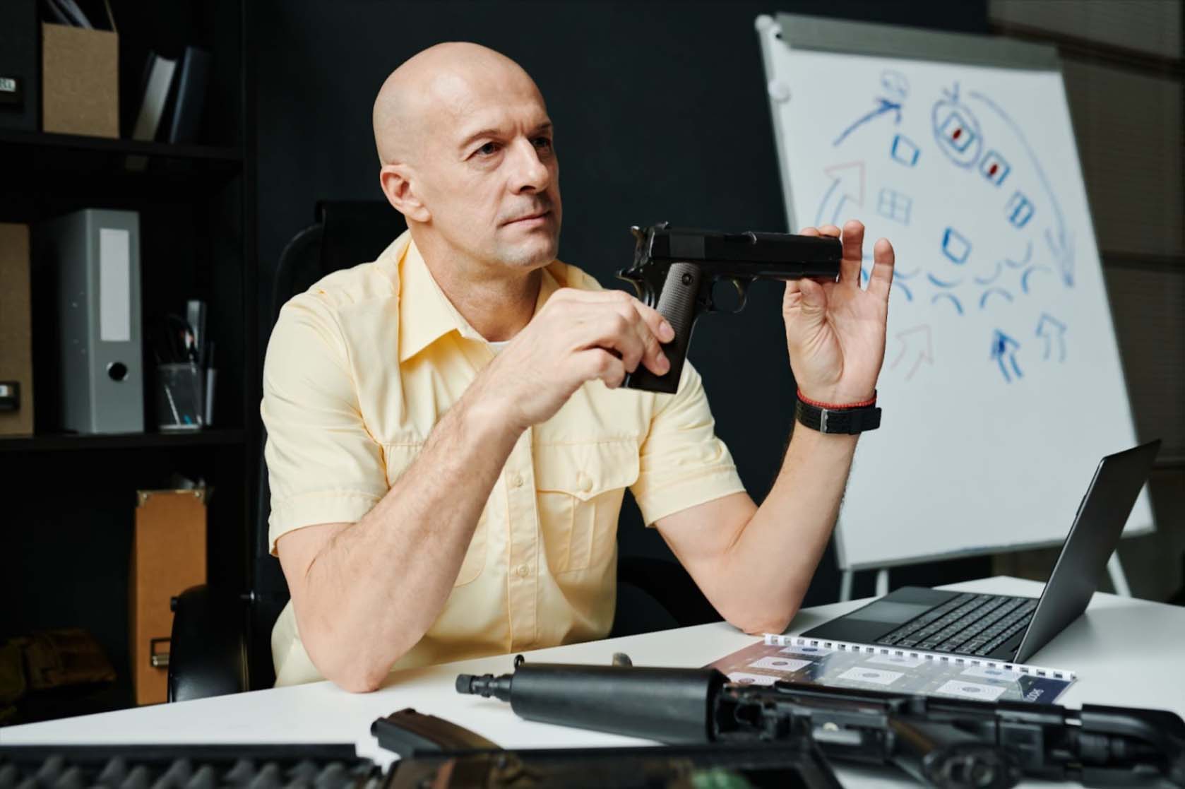 Bald, experienced male military trainer holding a sleek pistol with precision and confidence.