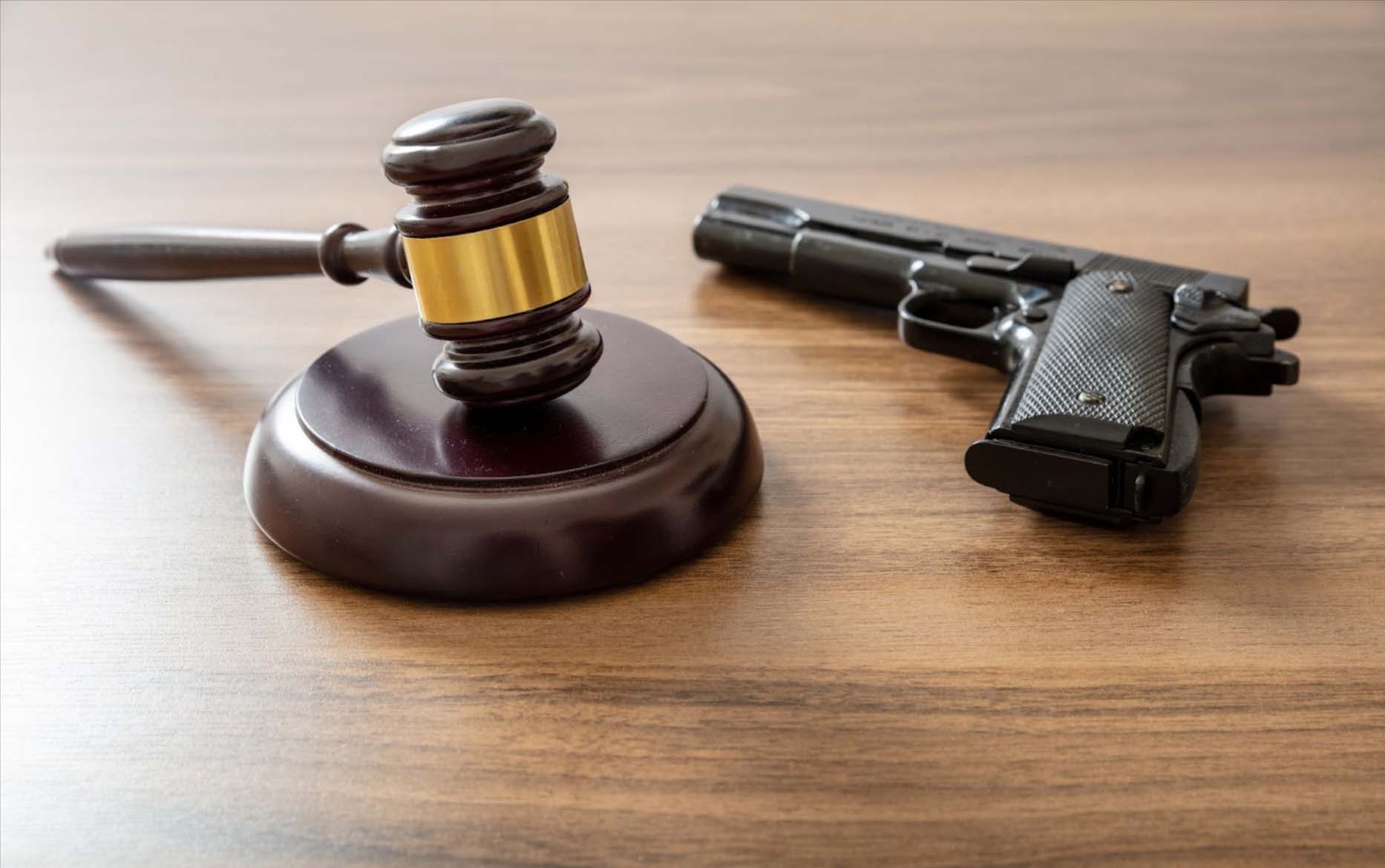 Close-up of a judge's gavel and handgun on a bench, symbolizing crime and punishment in legal firearms cases.