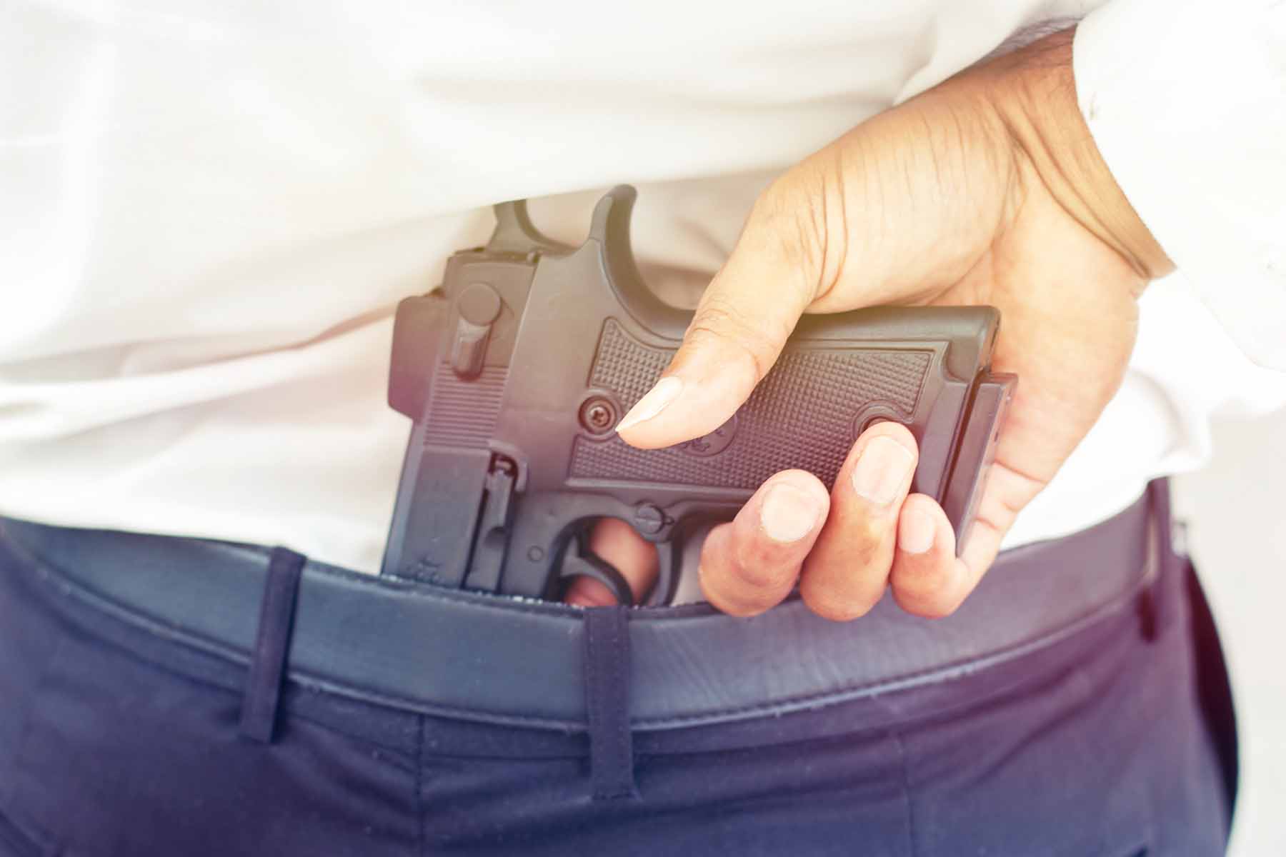 Cropped view of a man’s hand tucking his handgun into the back of his jeans.