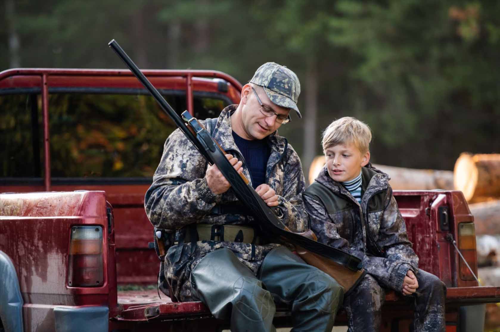 Dad showing his rifle to his son in a truck tailgate.