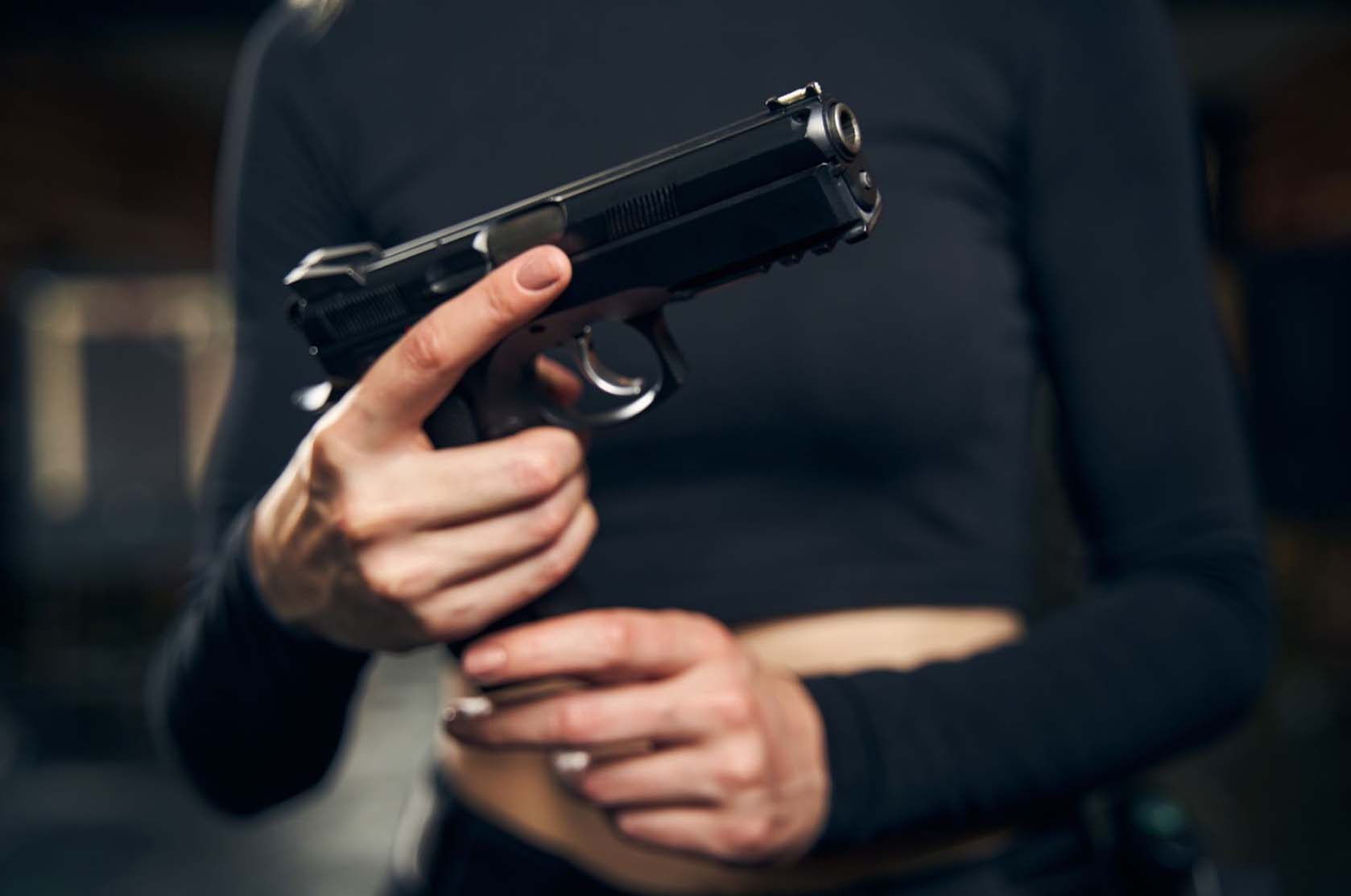 Female shooter, face obscured, readies her handgun for an indoor shooting drill.