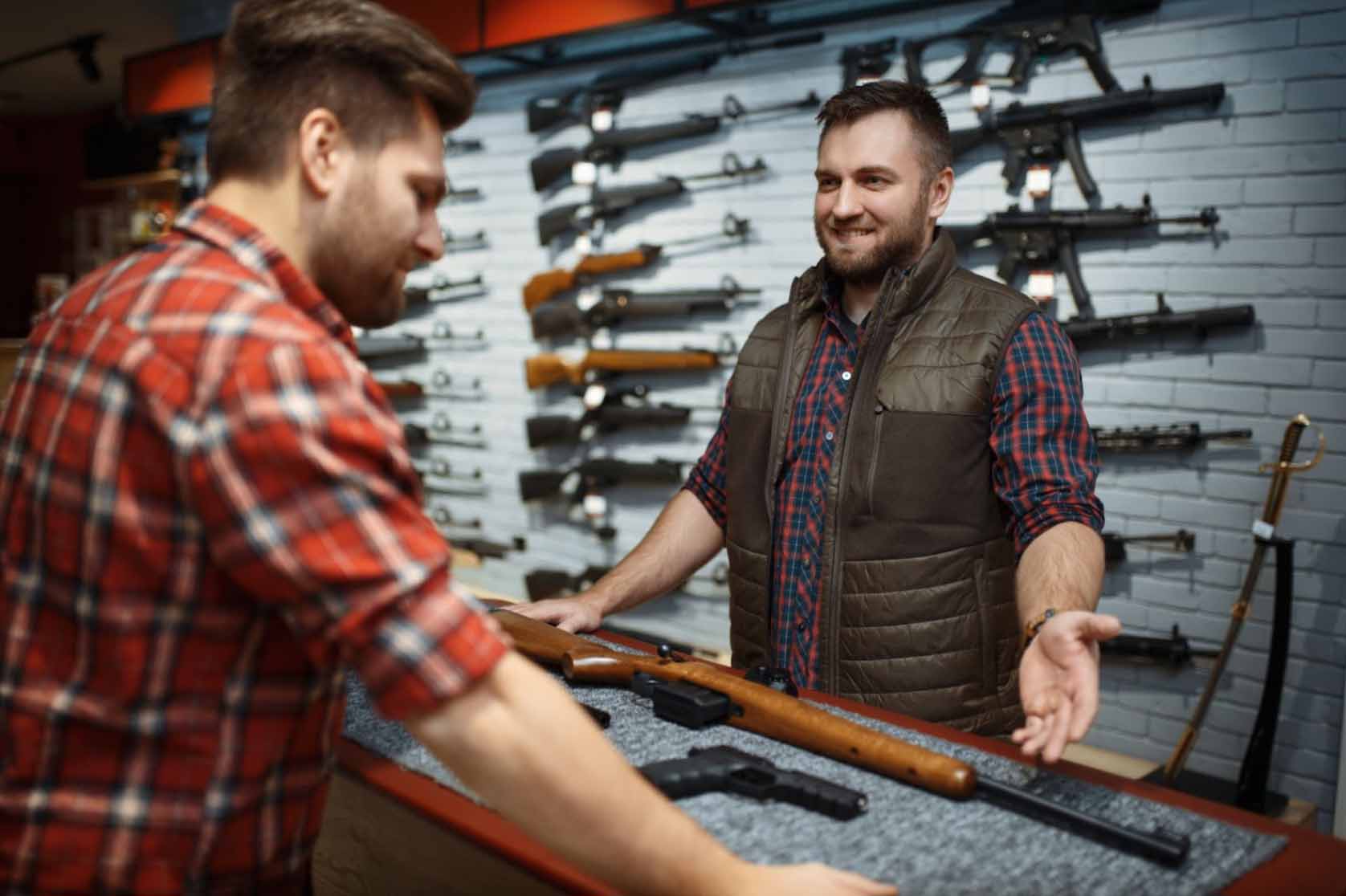 Shop owner showcases a rifle to a customer, demonstrating its features and craftsmanship.