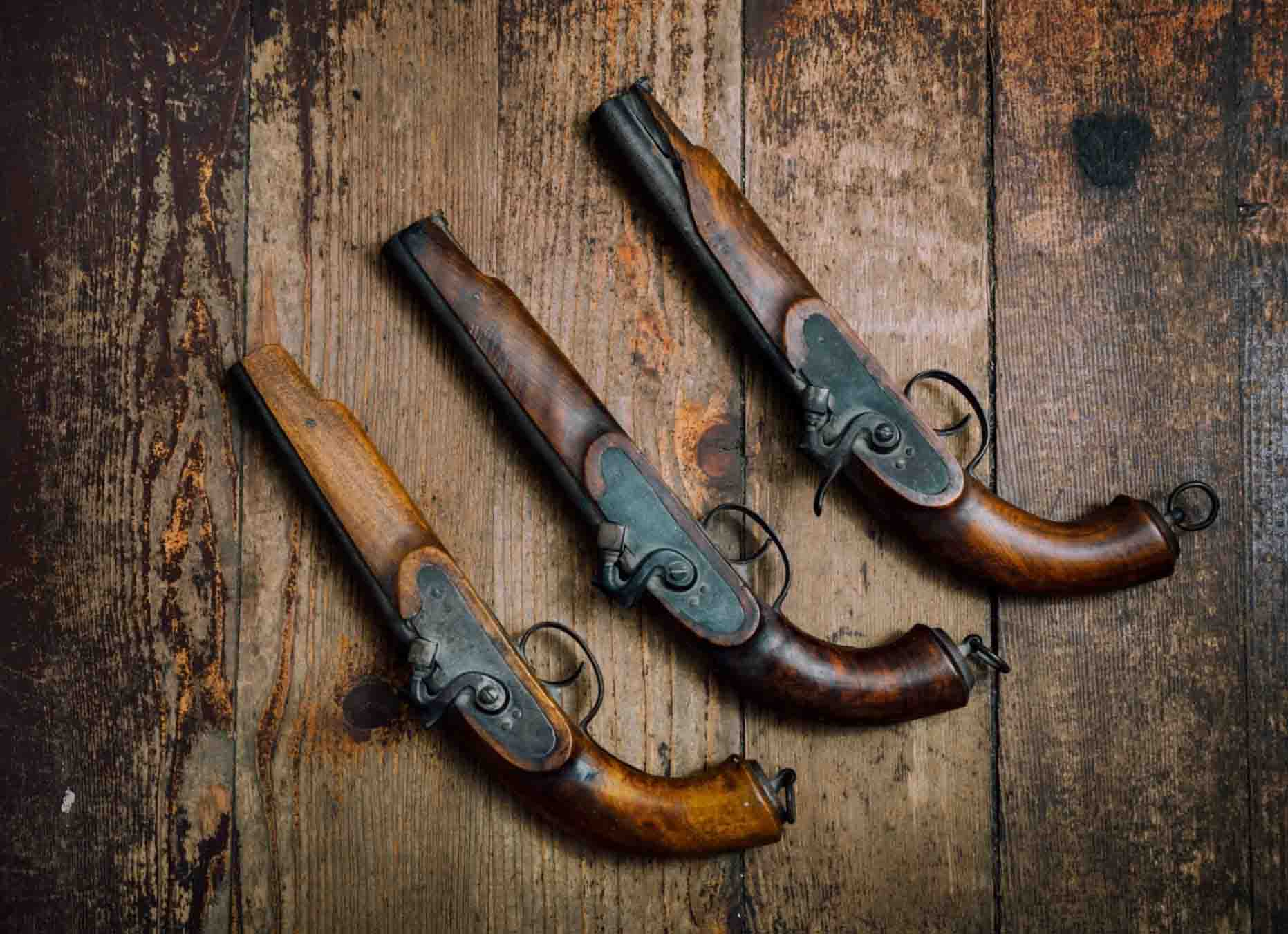 Three vintage brown pistols are displayed on a wooden table.