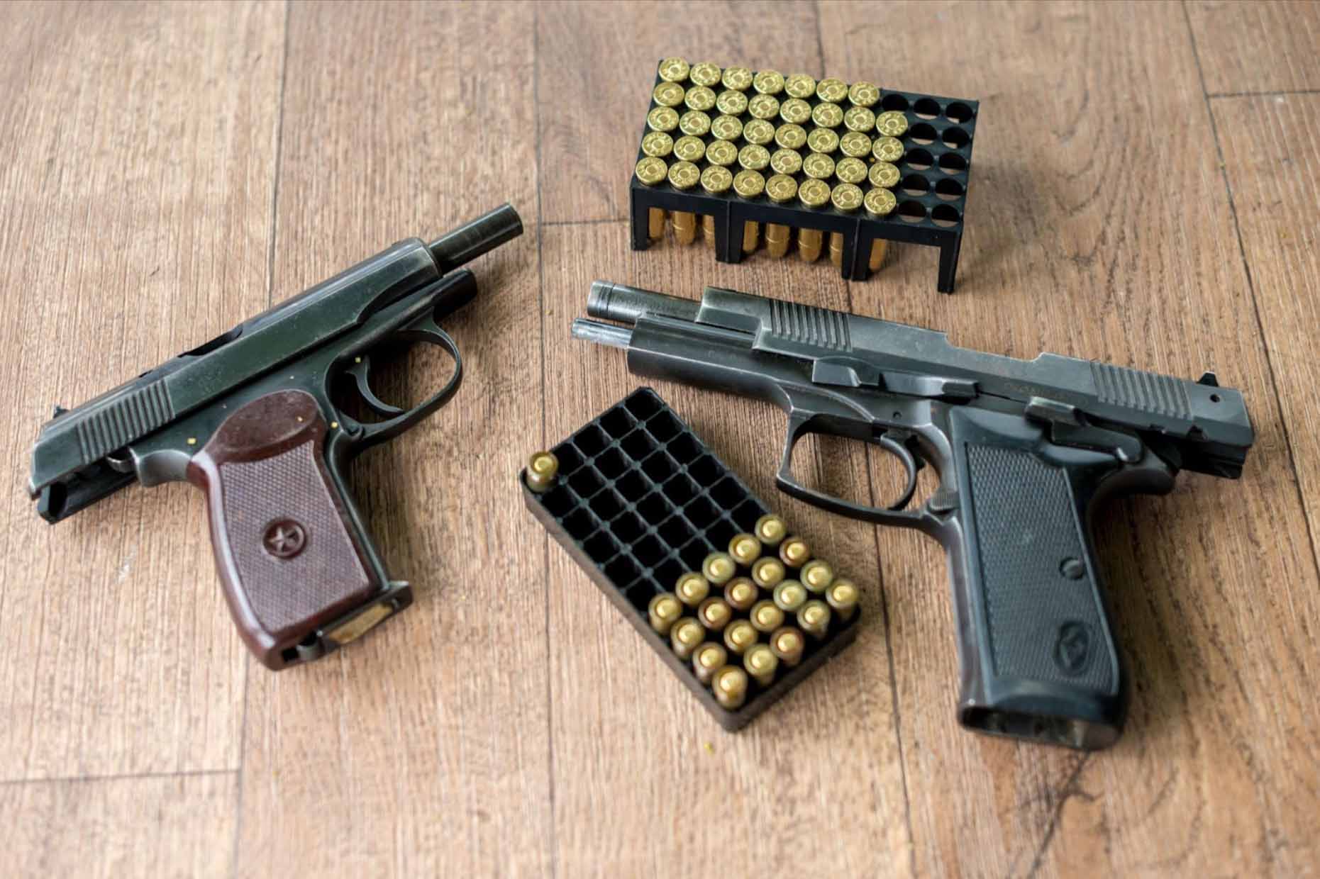 Two pistols and two ammunition packs neatly arranged on a wooden table.