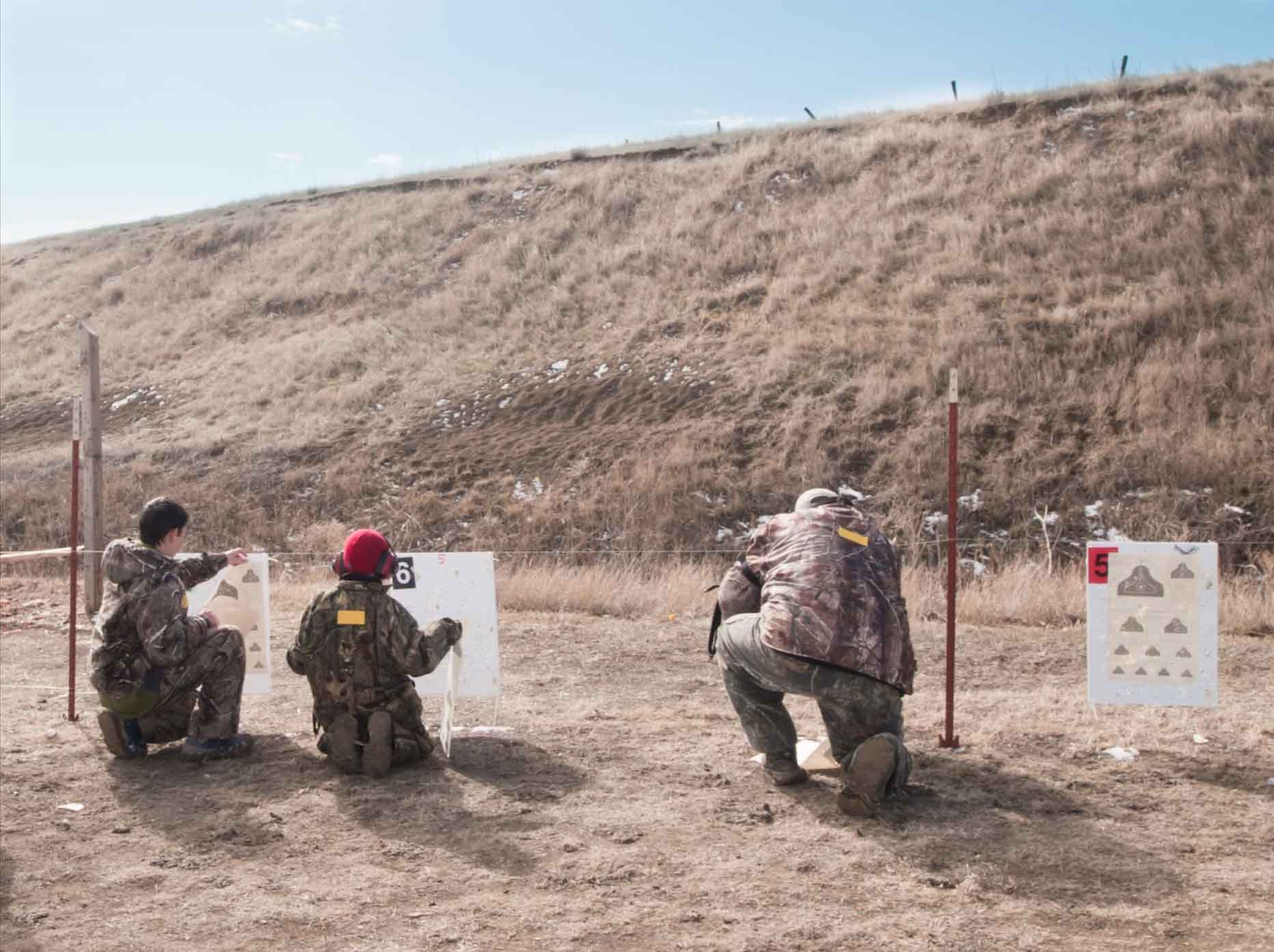 Two young boys and an adult examine their targets after shooting them.