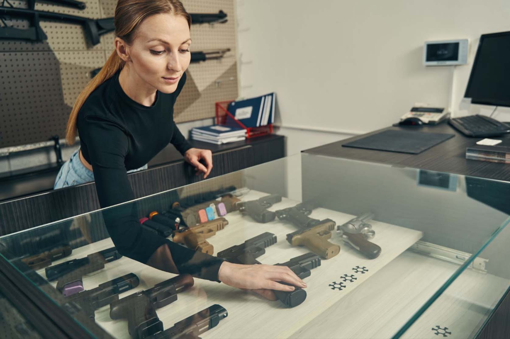 Woman reaching into a display case of guns.